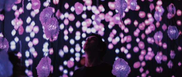 person standing below hanging purple light display in museum