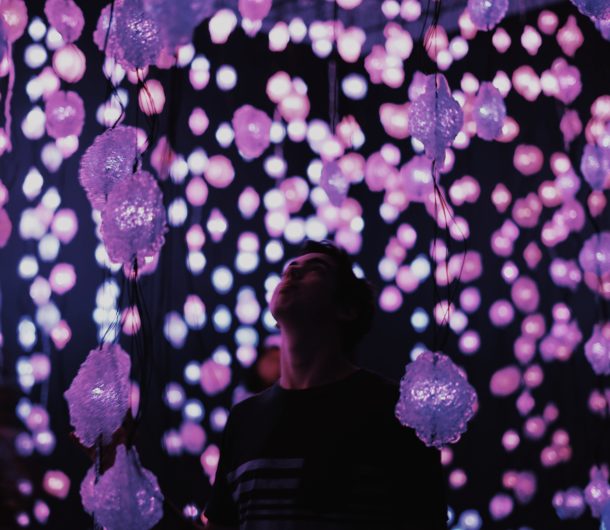person standing below hanging purple light display in museum
